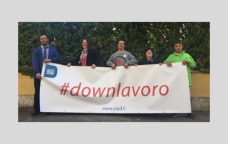 giovani con sindrome di Down tengono lo striscione con la scritta "#downlavoro"