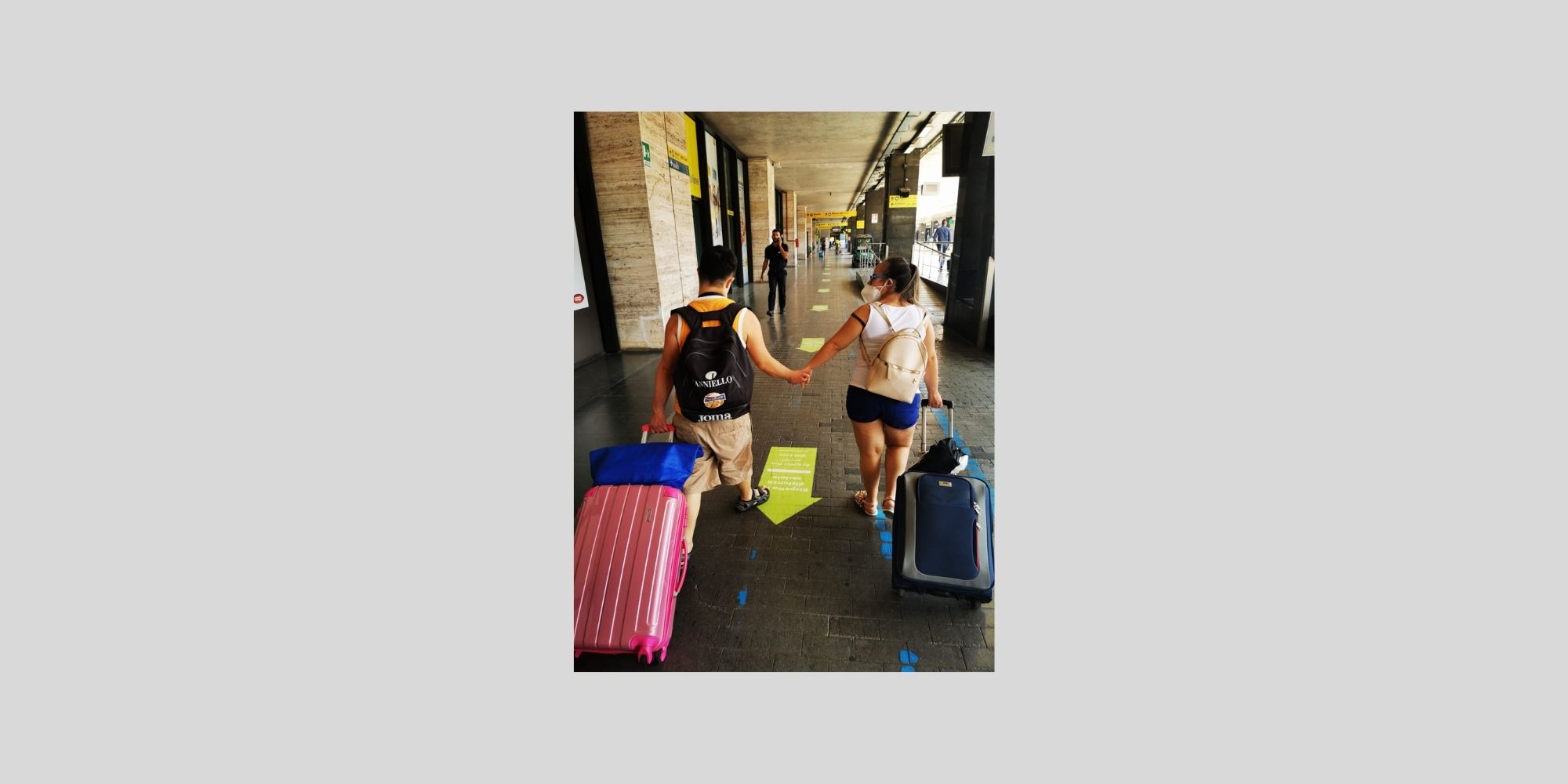coppia di giovani con sindrome di Down che si tengono per mano alla stazione con le valigie